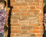 Un homme et une femme se tiennent de part et d'autre d'un mur de briques. Peut-on fixer quelque chose sur un mur mitoyen ?
