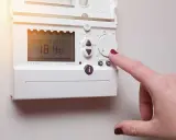 Main d'une femme ajustant un cee thermostat connecté affichant 18.4°C.