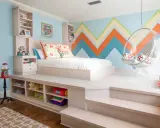 Chambre fille petit espace avec lit sur estrade, rangements intégrés, fauteuil bulle et mur géométrique coloré.