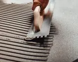 Application d'enduit pour carrelage avec une taloche crantée, assurant une épaisseur carrelage et colle uniforme pour une pose parfaite.