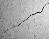 Gros plan sur une fissure traversant un plafond texturé. La fissure est sombre et profonde, contrastant avec la surface blanche et irrégulière.