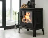 Poêle à bois en fonte avec flammes vives, pile de bois et accessoires. Idéal pour un couplage pompe à chaleur et poêle bois pour une chaleur optimale.