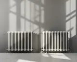 Deux radiateurs blancs classiques, parfaits pour reconnaître un radiateur haute température, projettent des ombres sur un mur gris.