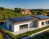 Une **petite maison passive** moderne avec des panneaux solaires sur le toit, entourée de verdure et de collines.