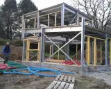 Chantier d'une maison ossature métallique. Le prix est un facteur clé pour ce type de construction moderne. Des tuyaux colorés sont visibles au sol.