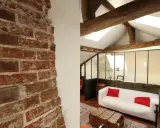 Aménagement combles idées : un salon cosy sous les toits avec murs en briques apparentes, poutres en bois et canapé blanc.