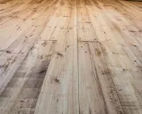 Planches de bois clair, usées et clouées, avec un parquet qui craque sous les pieds.