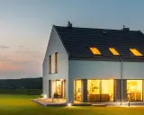 Une maison moderne et lumineuse, une maison autonome en France, avec de grandes fenêtres éclairées par une lumière chaude.