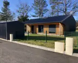 Maison passive ossature bois avec panneaux solaires sur le toit, bardage bois et métal, devant un ciel bleu et des arbres.