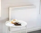 Un radiateur blanc moderne, idéal pour le chauffage maison neuve, avec une tasse de café et des magazines sur une table d'appoint.