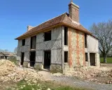 Construction d'une maison normande traditionnelle, avec colombages apparents et murs en pierre et brique. Le chantier est en cours.