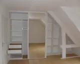 Aménagement astucieux pour faire un dressing sous pente. Étagères et tiroirs blancs s'intègrent parfaitement à l'espace mansardé.
