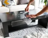 Mains appliquant un film adhésif marbré pour customiser une table basse noire.