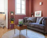Chambre d'amis confortable avec un canapé convertible (clic clac) en velours gris, des plantes vertes et un bureau mural.