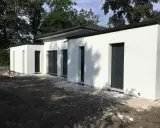 Maison moderne avec toit plat, plan de 150m2. Construction blanche aux lignes épurées, entourée d'arbres.