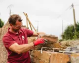 Un maçon, ganté de rouge, pose une pierre pour construire un mur en Corse.