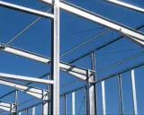 Structure métallique d'un bâtiment en construction, avec des poutres et des poteaux d'acier sous un ciel bleu clair.