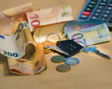 Clés, pièces et billets d'euros sur une table en bois. Calculatrice en arrière-plan. Le prix pose carrelage m2 est une préoccupation.