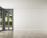 Un salon lumineux avec de grandes baies vitrées donnant sur un jardin verdoyant. Le parquet clair est parfait pour refaire le sol de la maison.