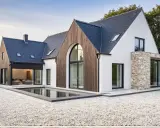 Une maison neuve en pierre et bois, avec une piscine rectangulaire devant.