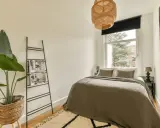 Chambre 9m2 avec salle de bain, lit douillet, plante verte et étagère murale. Luminaire en rotin au-dessus.