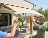 Deux hommes ajustent un store banne manuel avec un niveau à bulle pour un réglage parfait.