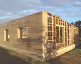 Construction d'une maison terre crue aux murs stratifiés, avec une ossature bois visible pour la suite.