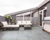 Terrasse moderne avec mobilier de jardin et barbecue. Le carrelage extérieur antidérapant est facile à nettoyer.
