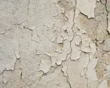 Texture d'un mur qui s'effrite, révélant des couches de peinture écaillée et des fissures profondes.