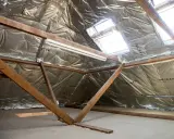 Isolation argentée sous les combles, avec poutres en bois et fenêtres de toit. Un système VMC sans comble est en cours d'installation.