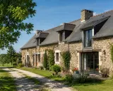 Longère moderne en pierre avec un chemin de gravier menant à l'entrée. Un jardin fleuri borde la façade.