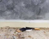 Outils pour enduire un mur abîmé : spatules et pot de mastic sur une bâche de protection au sol.