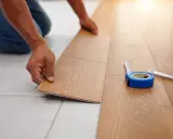 Pose d'un nouveau revêtement de sol imitation bois, une solution pour niveler un sol sans ragréage. Un mètre ruban et un cutter sont à proximité.