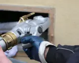Main d'un technicien en gant bleu tenant un raccord de remplissage pour une vieille chaudière fioul.