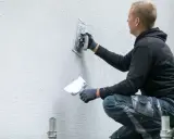 Artisan appliquant un enduit gratté sur un mur extérieur.