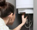Une femme vérifie le réglage de son chauffe-eau. Peut-on laisser un chauffe-eau en marche forcée ? La réponse dépend de votre appareil.