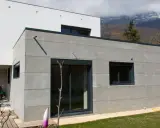 Extension moderne en parpaing gris, 20m2, avec grandes baies vitrées et vue sur montagnes.