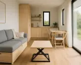 L'intérieur d'une maison container moderne avec un canapé gris, une cuisine et une table à manger. La lumière naturelle inonde la pièce par une grande baie vitrée.