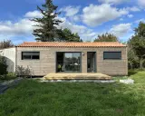 Une petite maison en bois avec une terrasse, idéale pour un plan maison 5m sur 10m. Le toit est couvert de tuiles rouges.