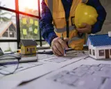Un architecte examine des plans pour une maison ancienne, évaluant le DPE. Maquettes de maisons sur la table.