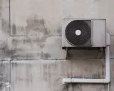 Unité extérieure d'une pompe à chaleur fixée sur un mur en béton. L'isolation est visible sur le tuyau blanc.