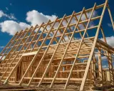 Charpente en bois d'une maison en construction, structure triangulaire sous un ciel bleu et nuageux.