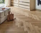 Un parquet en bois clair au calepinage en chevrons, avec un canapé, un sac et des lunettes posés dessus.