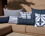 Plusieurs coussins bleus et blancs, à rayures et motifs tie-dye, sont disposés sur un canapé marron. Idée pour comment mettre un plaid sur un canapé.