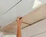 Mains installant des panneaux blancs pour refaire un plafond, avec un treillis visible en dessous.