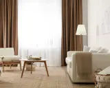 Salon cosy avec 1 ou 2 rideaux par fenêtre, fauteuil en bois, canapé blanc, table basse et tapis en jute.