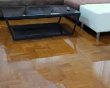 Un salon inondé, le parquet gondolé par l'eau. Une table basse et un pouf flottent dans le désastre.