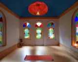 Un tapis de yoga orange attend dans une pièce lumineuse aux vitraux colorés, créant une atmosphère de maison bienveillante.