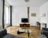 Salon moderne avec canapé gris, table basse en verre, bureau et mur blanc orné d'une carte de Paris.