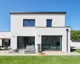 Maison moderne avec jardin, terrasse et chien. La ptz construction maison est visible sous un ciel bleu éclatant.